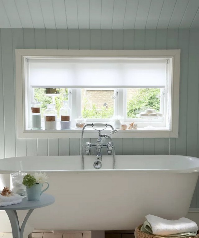 Велика біла ванна перед вікном і стіна, обшита світло-блакитними панелями